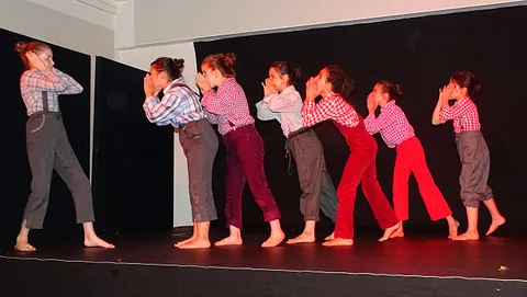 Eine Gruppe von Tänzerinnen in rosa Hemden und verschiedenen Hosen führt eine Choreographie auf.